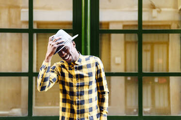 Smiling african man wearing hat against glass building - PGF00169