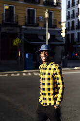 Confident african man with hands in pockets wearing hat in city - PGF00184