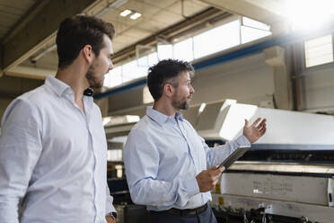 Reifer Geschäftsmann mit digitalem Tablet im Gespräch mit einem Kollegen, während er in einer Fabrik steht - DIGF12961
