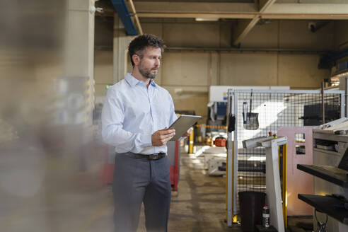 Geschäftsmann mit digitalem Tablet, der in einer Fabrik stehend Produktionsanlagen untersucht - DIGF12962