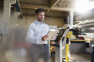 Mature businessman using digital tablet while standing at factory - DIGF12963