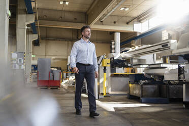 Businessman looking at manufacturing machine while walking at factory - DIGF12964