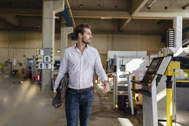 Junger Geschäftsmann hält Aktentasche beim Spaziergang in einer Fabrik - DIGF12965