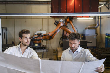 Businessmen holding blueprint paper while standing against automated machine at factory - DIGF12978