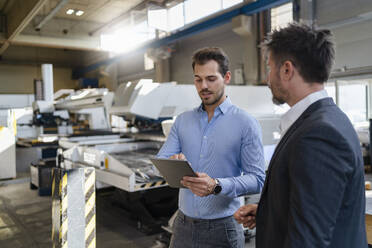 Businessman using digital tablet while standing by colleague at factory - DIGF12994