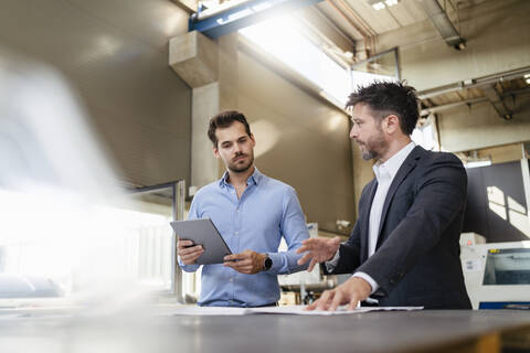 Businessman discussing with colleague holding digital tablet while standing at factory stock photo