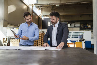 Junger Geschäftsmann mit digitalem Tablet bei der Arbeit, während er neben einem Kollegen in einer Fabrik steht - DIGF13000