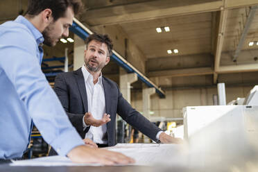 Businessman and colleague discussing blueprint while standing at factory - DIGF13004