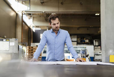 Young businessman analyzing blueprint while standing by table at factory - DIGF13005