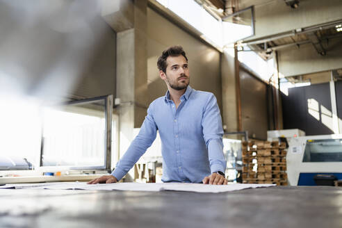 Geschäftsmann schaut weg, während er an einem Tisch in einer Fabrik steht - DIGF13006