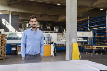 Confident businessman with hands in pockets standing by table at factory - DIGF13009