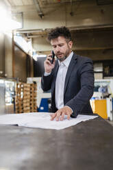 Businessman wearing suit talking on mobile phone while working at factory - DIGF13012