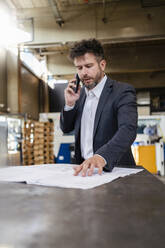 Geschäftsmann im Anzug, der bei der Arbeit in einer Fabrik mit seinem Handy telefoniert - DIGF13012