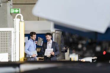 Businessman holding paper having discussion with colleague while standing at factory - DIGF13019