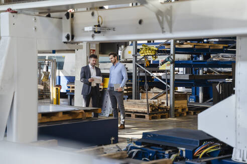 Geschäftsmann hält Papier, während er einem Kollegen in einer Fabrik etwas erklärt - DIGF13021