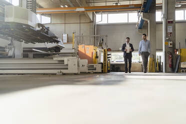 Businessman with digital tablet looking away while walking by colleague at factory - DIGF13026