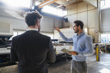 Young man using digital tablet while discussing with colleague at factory - DIGF13030