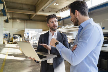 Businessmen working on laptop while standing at factory - DIGF13031