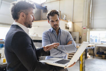 Mature man using laptop while standing by colleague at factory - DIGF13032