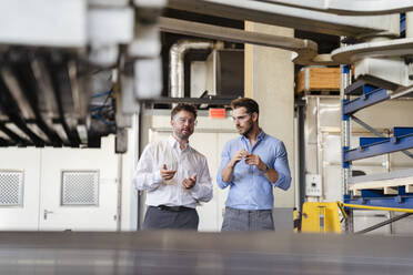 Businessmen having discussion while standing by equipment at factory - DIGF13040