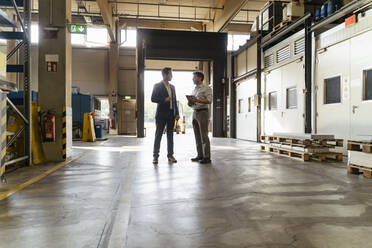 Businessman discussing with colleague while standing at factory - DIGF13043