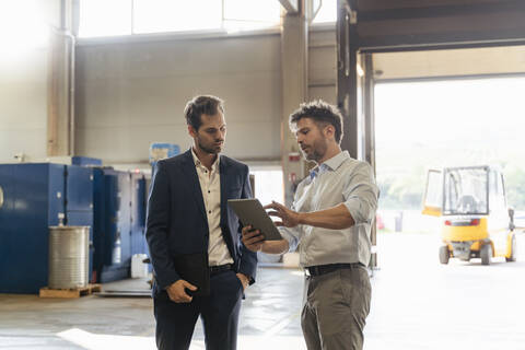 Mature man using digital tablet while discussing with businessman at factory stock photo