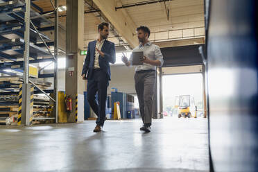 Businessman and colleague with digital tablet talking while walking at factory - DIGF13045