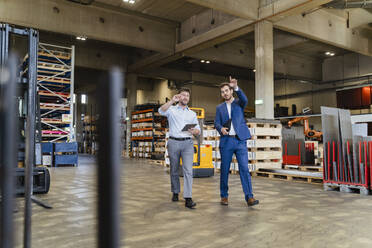 Businessman examining warehouse with colleague while walking at factory - DIGF13047