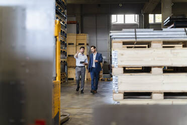 Businessman and colleague inspecting warehouse while walking at factory - DIGF13048