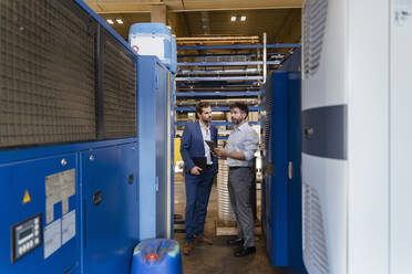 Businessman and colleague with digital tablet examining equipment while standing at factory - DIGF13051