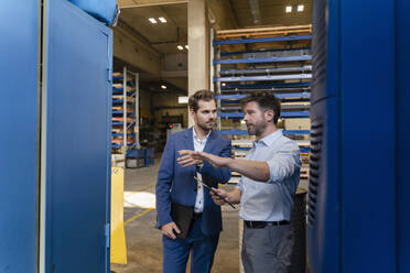 Businessman and colleague with digital tablet having discussion while standing at factory - DIGF13052