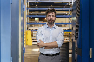 Businessman standing with arms crossed at warehouse in factory - DIGF13053