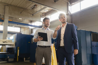 Colleague using digital tablet while having discussion with businessman at factory - DIGF13056