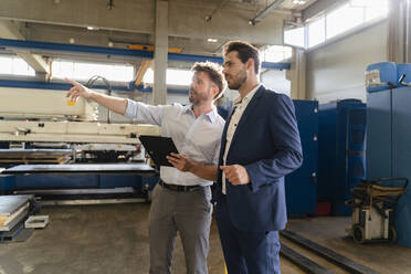 Geschäftsmann hält digitales Tablet bei der Arbeit, während er neben einem Geschäftsmann in einer Fabrik steht - DIGF13057