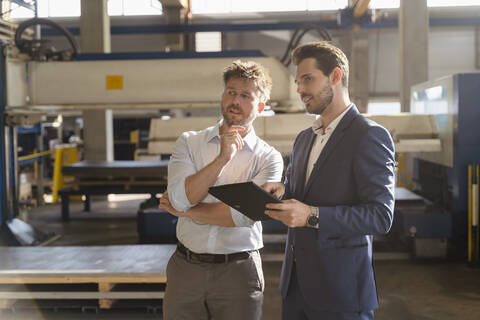 Businessmen with digital tablet looking away while standing at factory stock photo