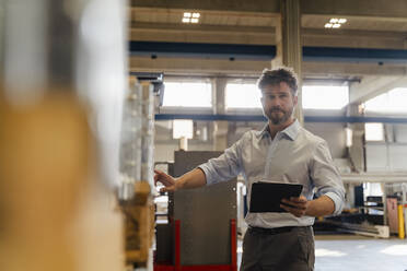 Männlicher Inspektor, der ein digitales Tablet benutzt, während er Material im Lager einer Fabrik überprüft - DIGF13069