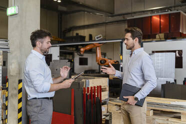 Geschäftsmann mit digitalem Tablet im Gespräch mit einem Kollegen, während er in einer Fabrik steht - DIGF13073