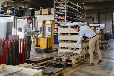 Business people inspecting metal material while standing at warehouse in factory stock photo