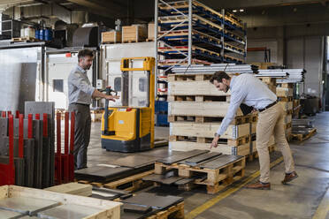 Geschäftsleute inspizieren Metallmaterial, während sie in einem Lagerhaus in einer Fabrik stehen - DIGF13078