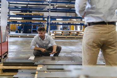 Businessman checking metal while working with colleague at factory - DIGF13079