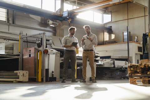 Businessman with digital tablet standing by colleague checking metal object at factory stock photo