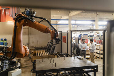 Business people having discussion while standing by automated robotic arm at factory - DIGF13092