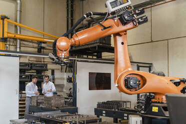 Automatic robotic arm machine with businessmen standing in background at factory - DIGF13094