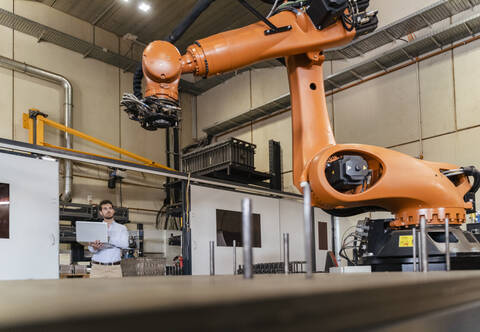 Young businessman with laptop examining automatic robot arm machine at factory stock photo