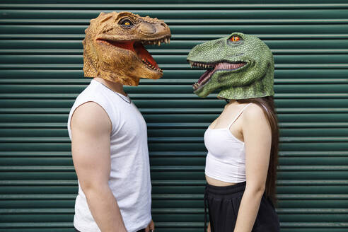 Männlich und weiblich mit Dinosauriermaske vor grünem Fensterladen - IFRF00001