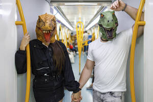 Männliche und weibliche Freunde halten sich an den Händen und tragen Dinosauriermasken im Zug - IFRF00009