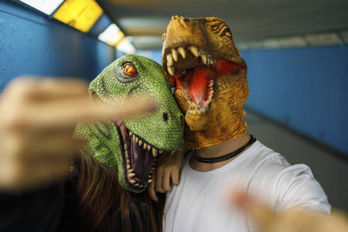Männliche und weibliche Freunde zeigen den Mittelfinger, während sie eine Dinosauriermaske im Korridor tragen - IFRF00015