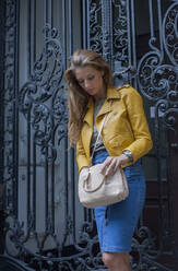 Beautiful woman checking purse while standing in front of metallic gate - AJOF00505