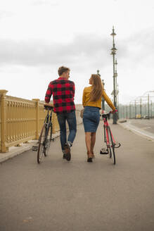 Lächelndes heterosexuelles Paar mit Fahrrad auf dem Gehweg in der Stadt - AJOF00512