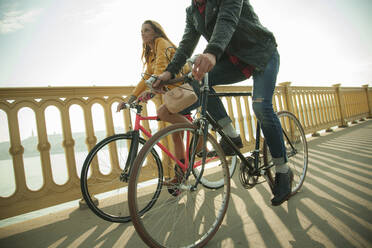 Heterosexuelles Paar fährt Fahrrad auf einer Brücke gegen den Himmel - AJOF00514